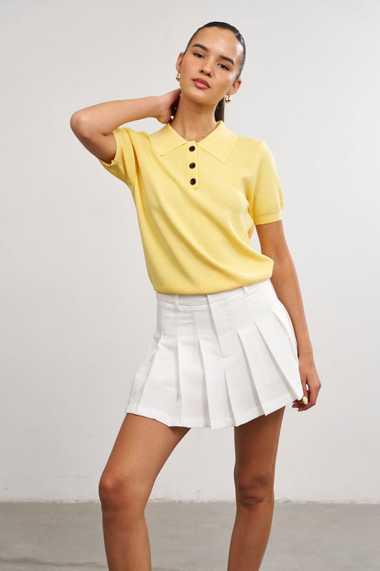 דוגמנית לובשת פולו צהובה וחצאית לבנה